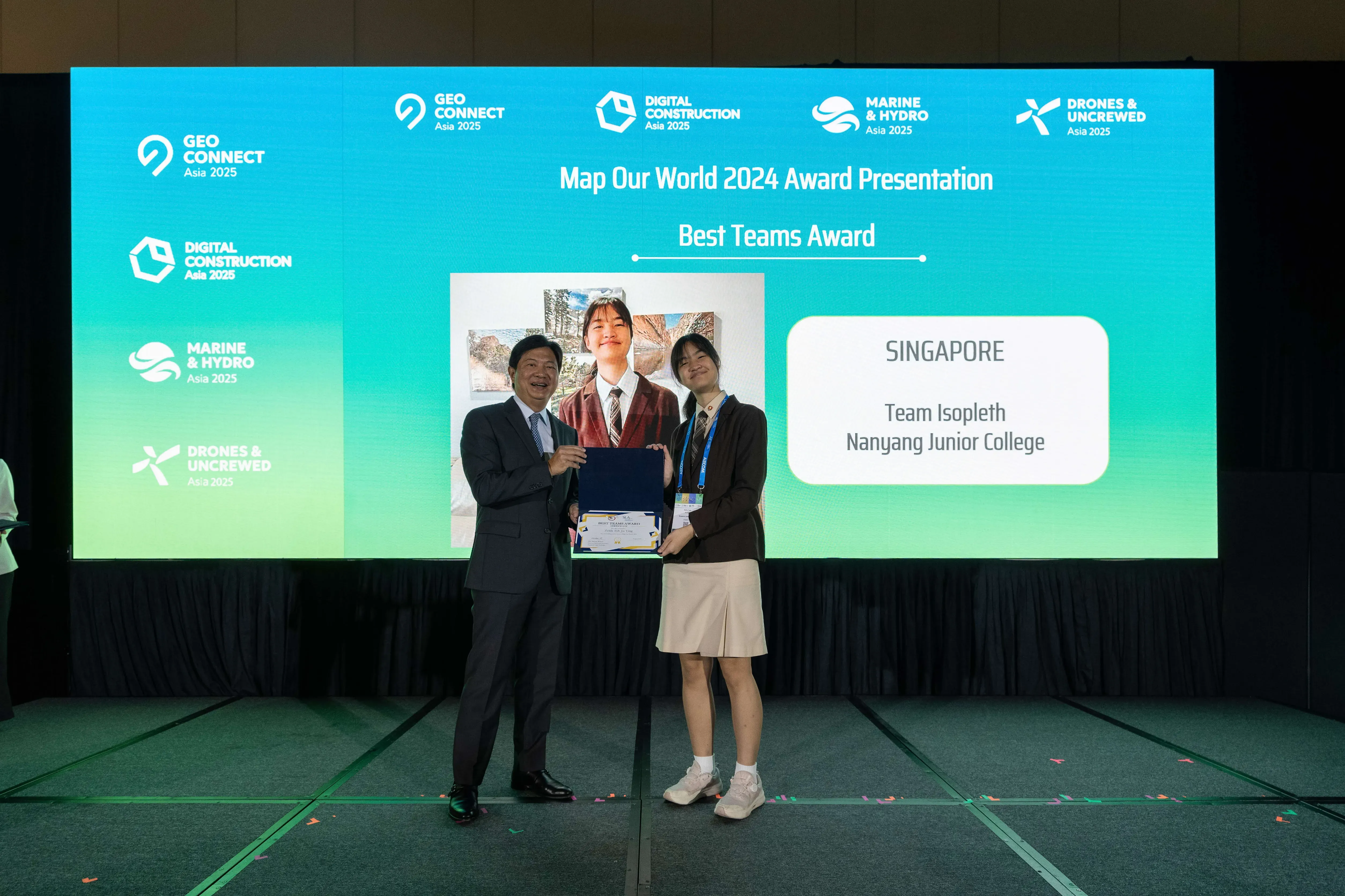 Two people hold a certificate on stage at the Map Our World 2024 Best Teams Award for Singapore's Nanyang Junior College.